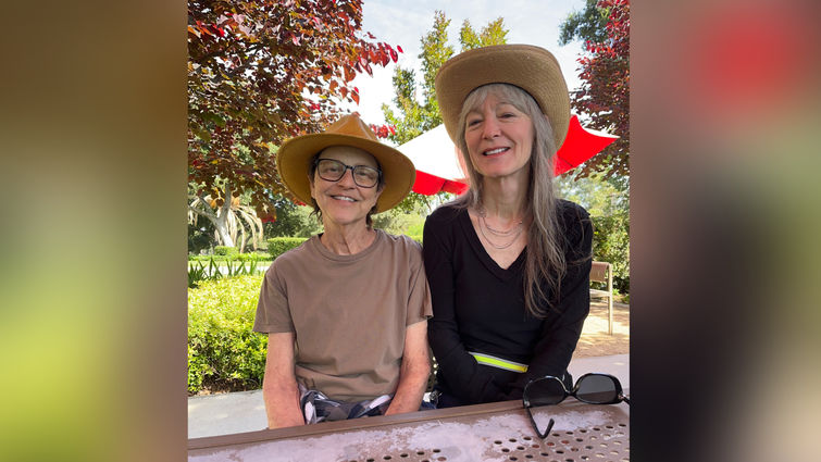 Two Caucasion women sitting outside, smiling, wearing sun hats