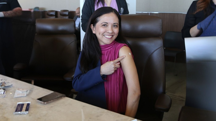 LLUH CFO Angela Lalas is all smiles after getting her flu vaccine A women smiles at the camera and points to a bandaid on her arm
