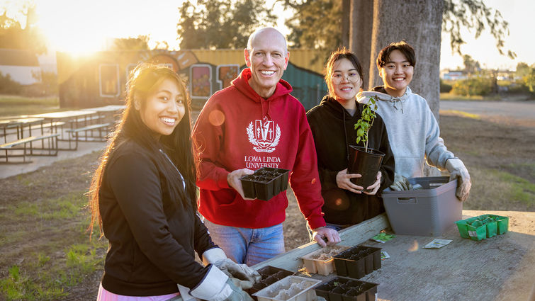 four individuals smiling, gardening at a table outside in hoodie sweatshirts