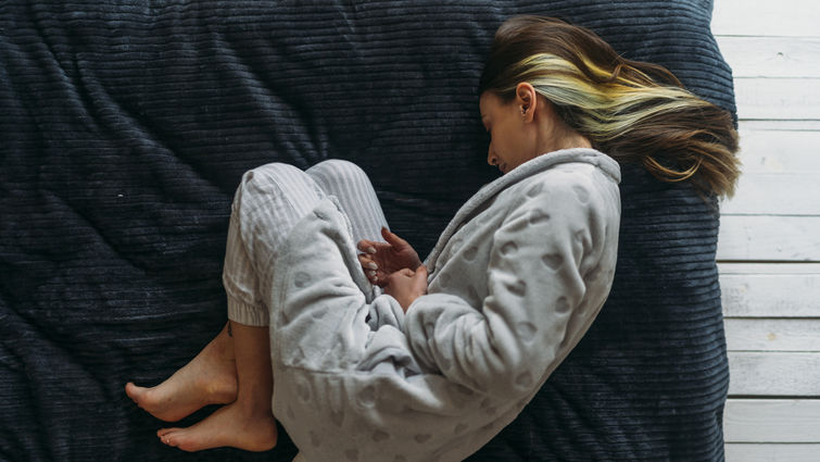 Caucasian woman laying on her side holding her stomach. Photo taken from above