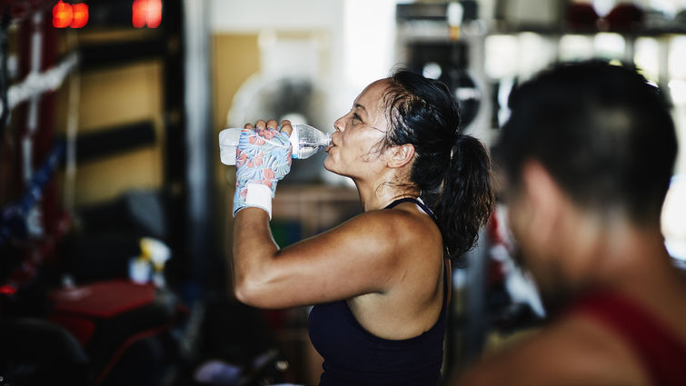 Sweating female boxer drinking water after workout in boxing gym - stock photo