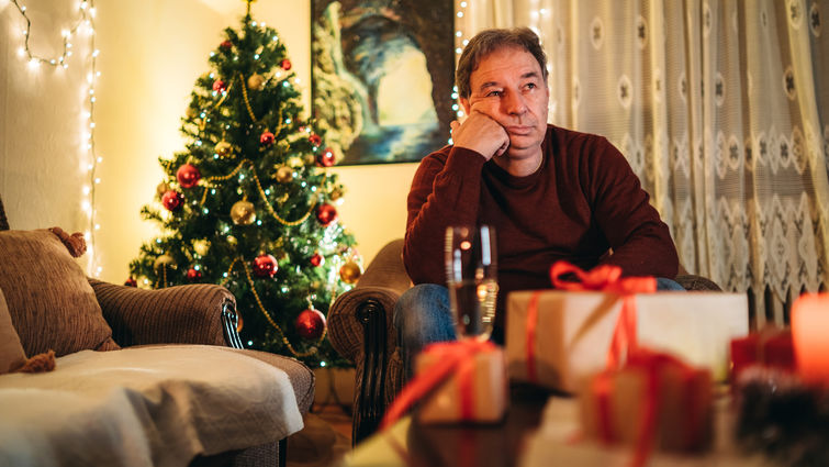 Senior caucasian man sitting on a couch and waiting alone for Christmas / New Year's eve.