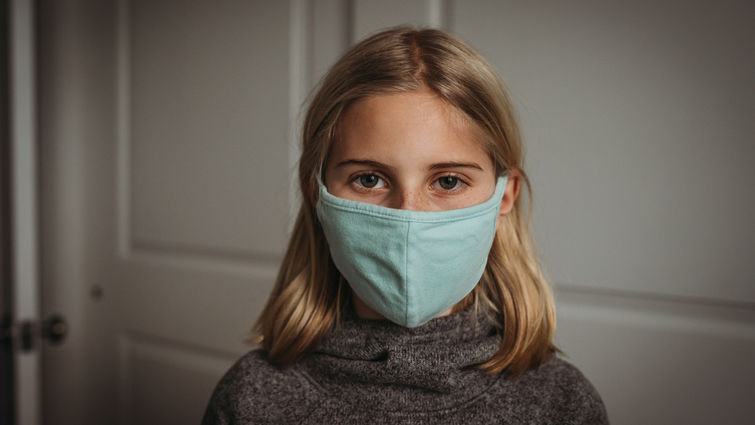 Girl in face mask looking at camera during Covid-19 pandemic - stock photo