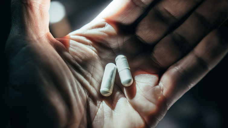 Hands holding pills in dramatic light. - stock photo