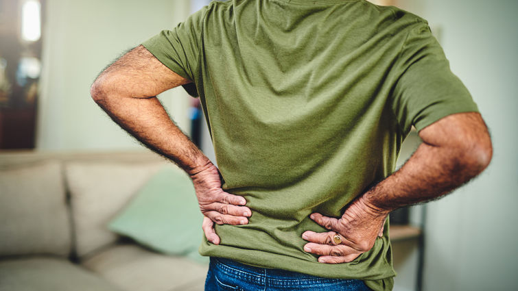 Cropped shot of a senior man in a green shirt holding his lower back suffering from back pain