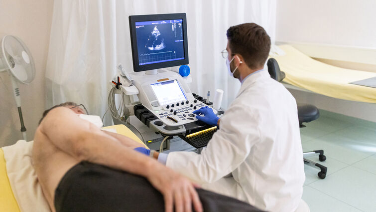 Doctor looking at the computer screen while doing an ultrasound test of a senior male patient lying on clinic bed during pandemic. Cardiologist doing heart ultrasound of an elderly man in hospital.