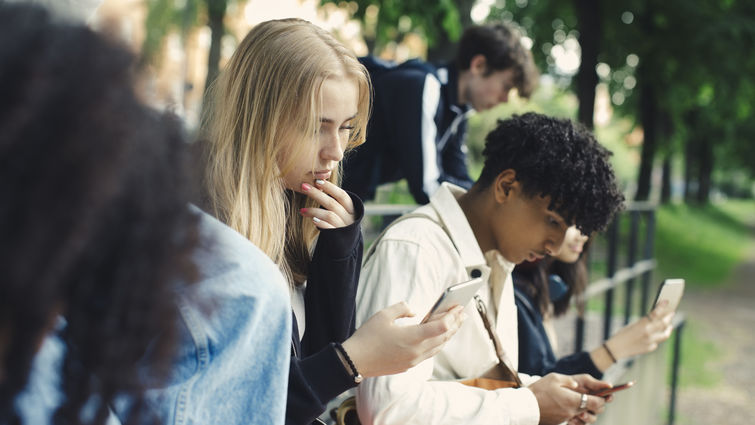 Male and female friends using smart phones in park - stock photo