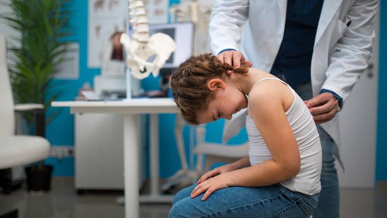 Pediatrician doing development medical exam with little girl, checking spine