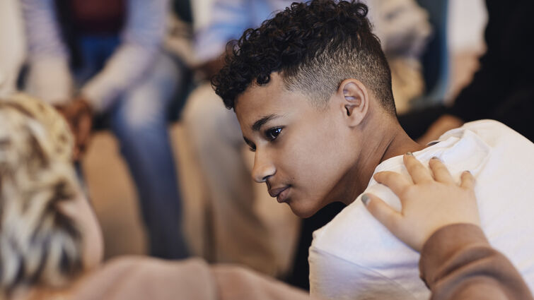 Teenage boy looking at female friend consoling in group therapy