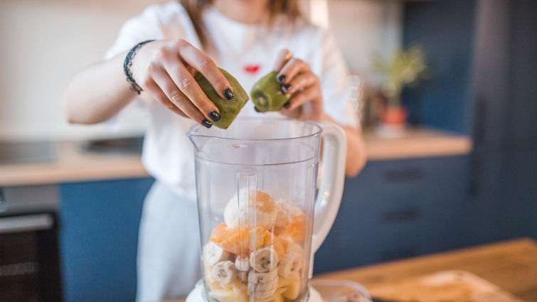 Woman puts kiwi in a blender - stock photo