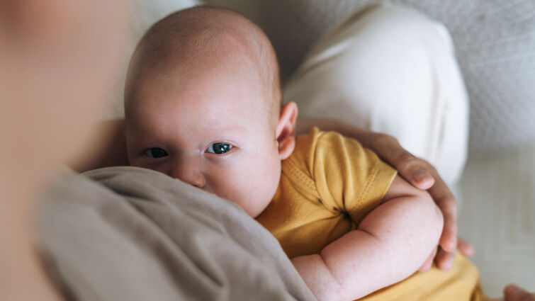 Young mother breastfeeding your 2-3 month baby boy lying on blanket at home