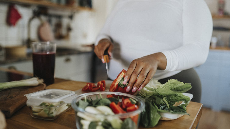 Midsection of young woman cutting red bell pepper while preparing salad in kitchen at home