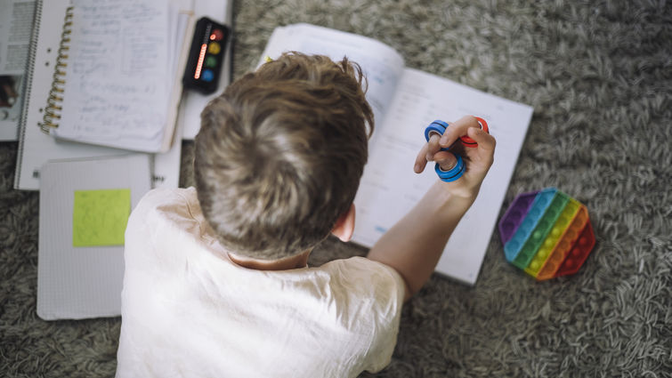 Directly above view of boy fidgeting with ring toys while doing homework at home