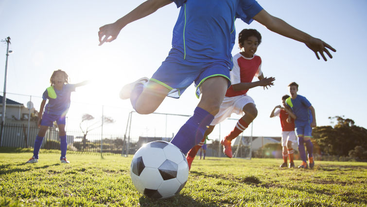 Close up of boy wearing a blue soccer uniform kicking soccer ball 