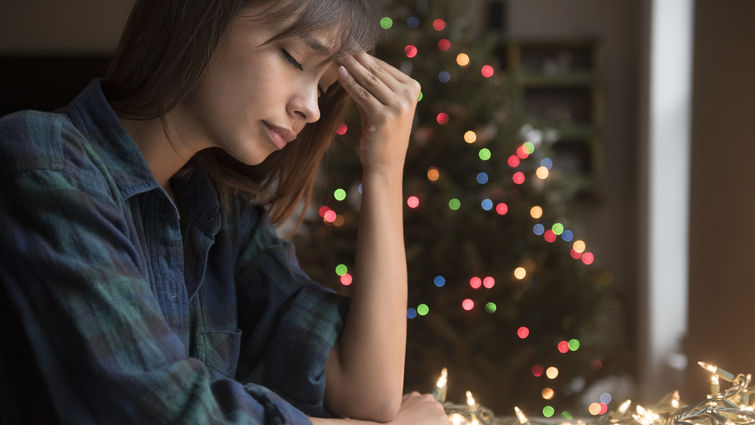 Women with her head on her hand in sadness with a Christmas tree in the background