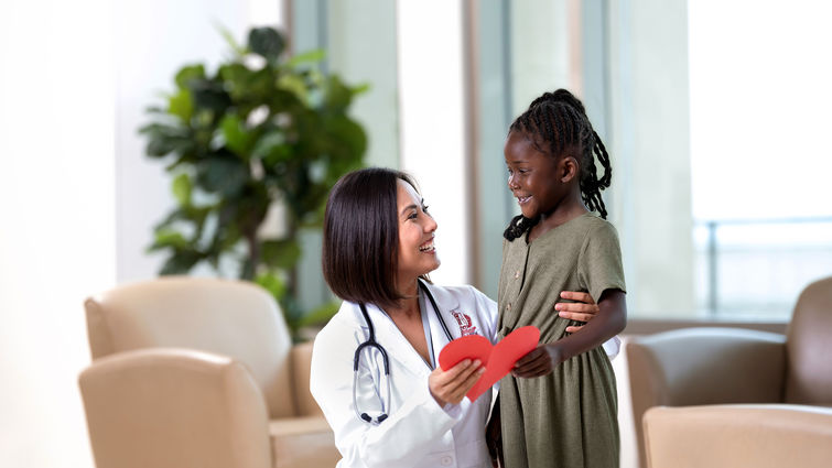 Female physician with young Black female holding a red paper heart