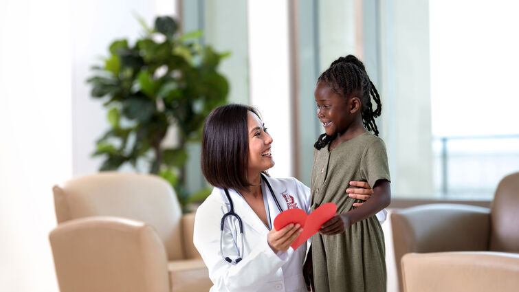 Female physician with young Black female holding a red paper heart
