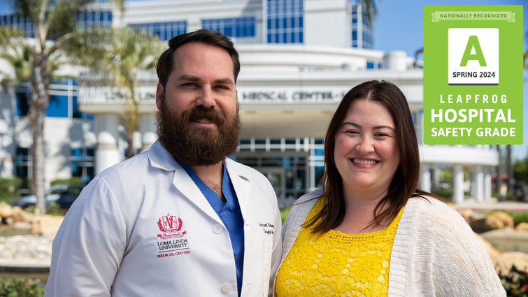 Brown-haired Caucasian male with a beard wearing a white coat standing next to a brunette in a yellow blouse outside 