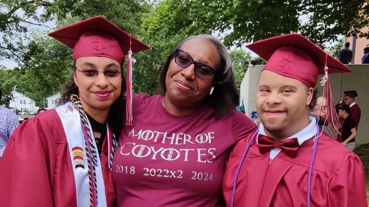 Luann smiling proudly standing with her two high school graduates, Diviana and Alexavier, who are in their graduation regalia