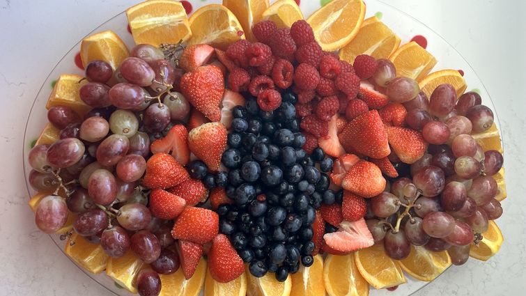 A tray of grapes, oranges, strawberries, and blueberries sitting on a white table