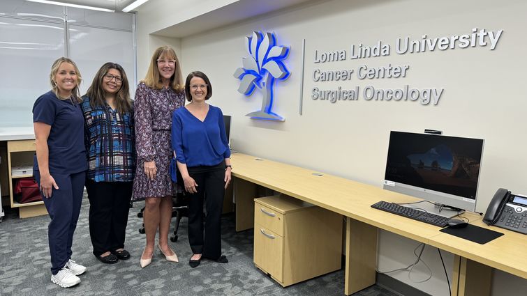 Four women stand to the left and pose next to a wall sign reading "Loma Linda University Cancer Center Surgical Oncology"