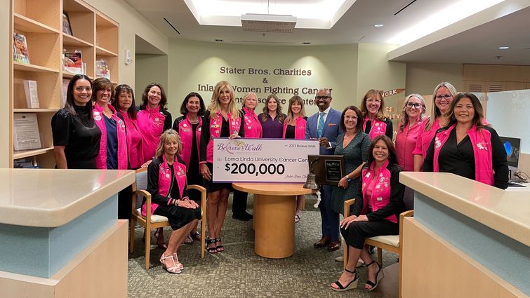 Group of people wearing pink in honor of breast cancer awareness month, during a check presentation with a large check for $200,000