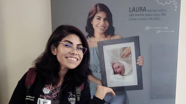 Nurse Laura stands in front of hallway image of herself holding a photo of newborn Laura when she was in NICU