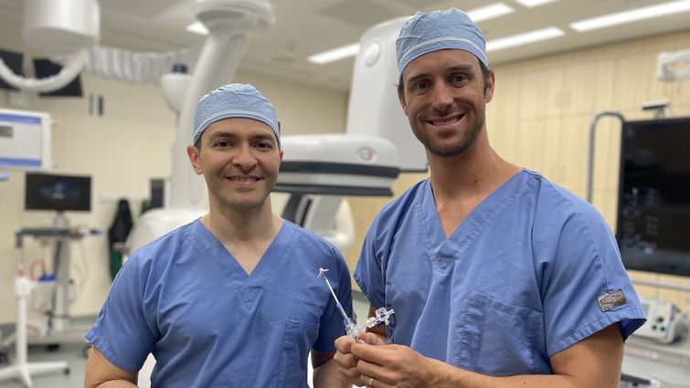 Structural interventional cardiologists Drs. Amr Mohsen (left) and Jason Hoff (right) hold the device they used to perform Gail Perszyk's mitral transcatheter edge-to-edge valve repair.