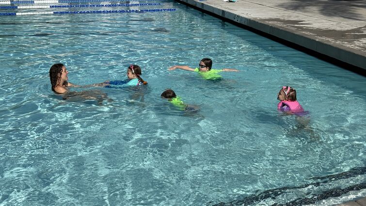 Four kids swimming towards swim instructor at the Drayson Center pool