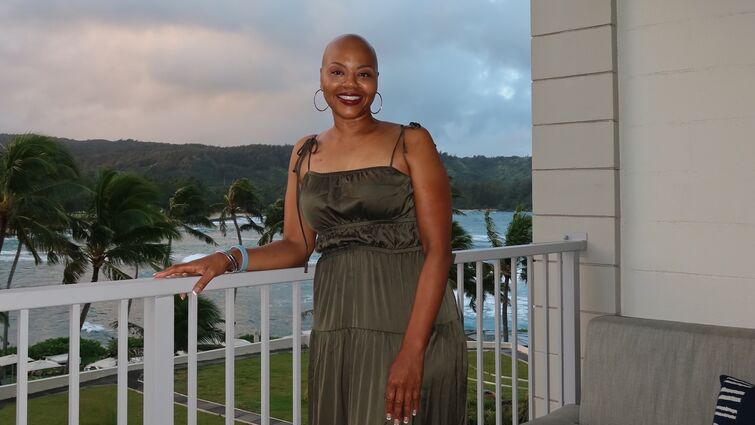 Sonja Loadholt stands on balcony overlooking beach and palm trees