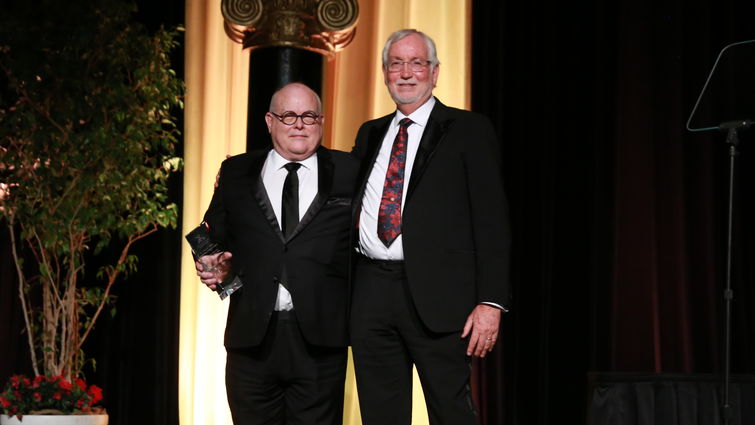two doctors standing on stage, one holds award, both smiling