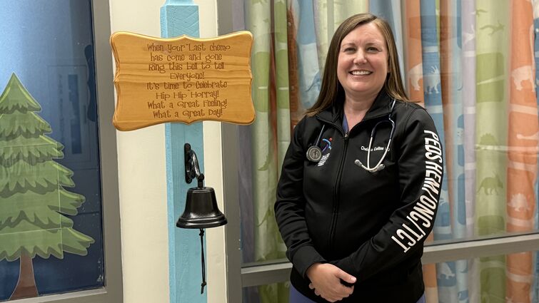 Dr. Chelsea Collins stands beside the cancer-free bell in the pediatric oncology unit at Loma Linda University Children’s Hospital Dr. Chelsea Collins standing next to cancer-free bell
