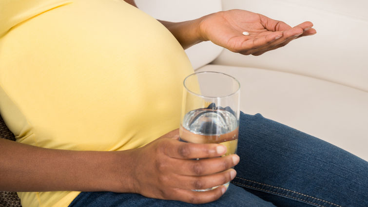 pregnant woman in yellow shirt holding glass of water and small white pill