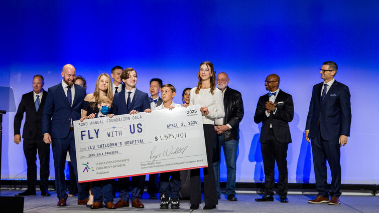 Hospital leadership, staff, and patient stand on stage holding large check with total number of funds raised at charity event
