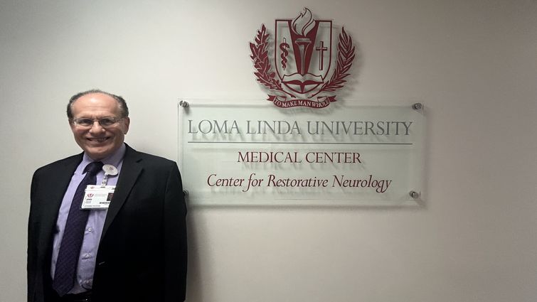 man standing in suit smiling in front of sign that reads loma linda university medical center center for restorative neurology 