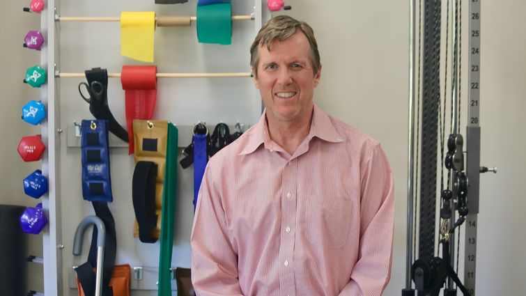 Mark Bussell, DPT, sits in front of physical therapy equipment