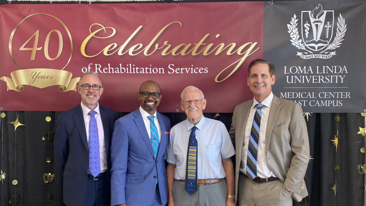 Four men stand in front of banner that reads "Celebrating 40 years of Rehabilitation Services"