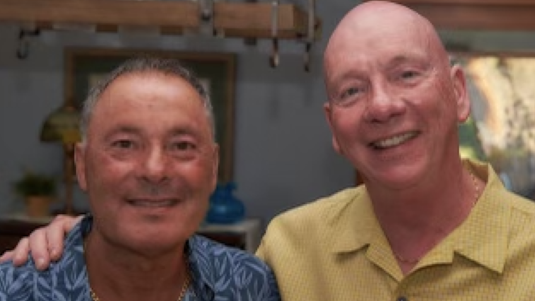 Two Caucasion men smiling side by side, one in a blue shirt, the other in yellow.