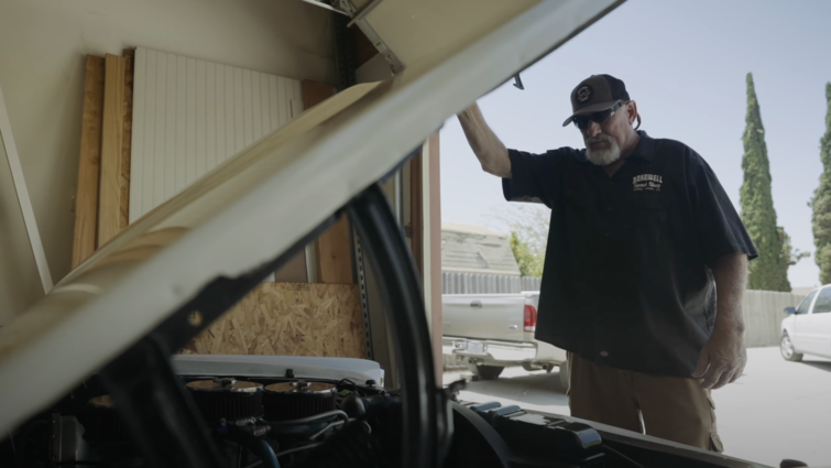 Man stands looking in hood of vintage car.