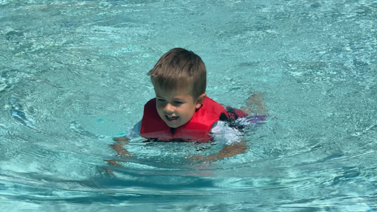 Young boy swims in pool with US Coast-guard approved life vest