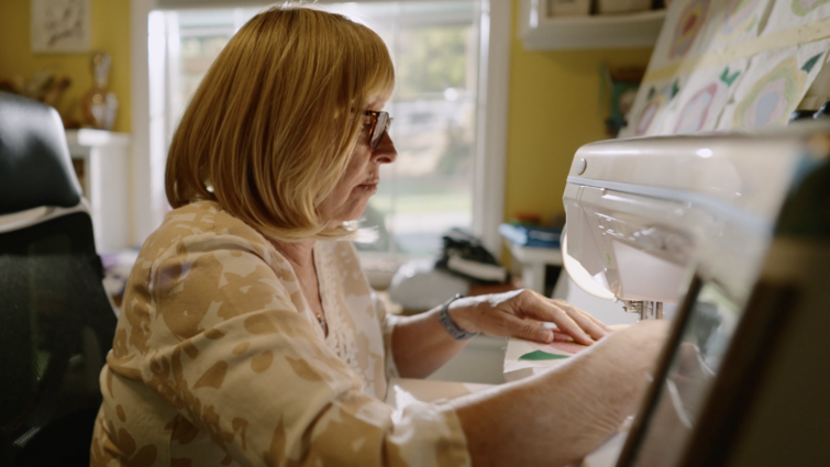 Breast cancer patient Phyllis Zehms says she’s living proof of the importance of preventive care. A woman is sitting in a chair using a sewing machine