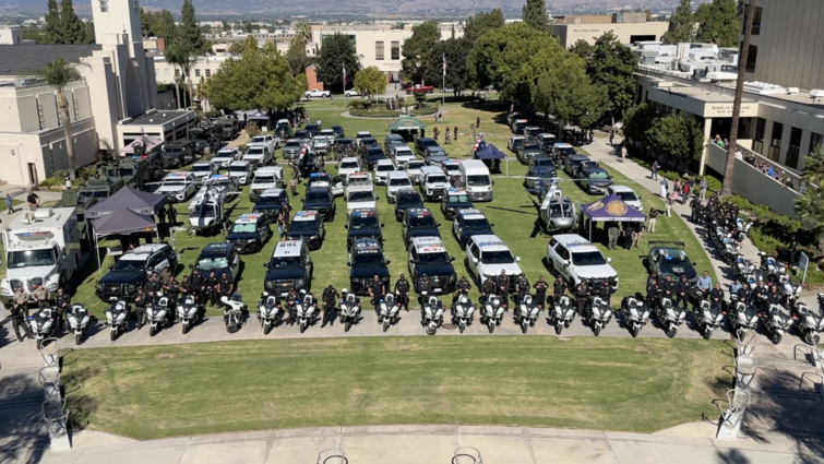 Aerial view of the Loma Linda University campus north lawn filled with rows of police vehicles, motorcycles, and officers from various Southern California law enforcement agencies during the 24th Annual Cops for Kids Fly-In event.