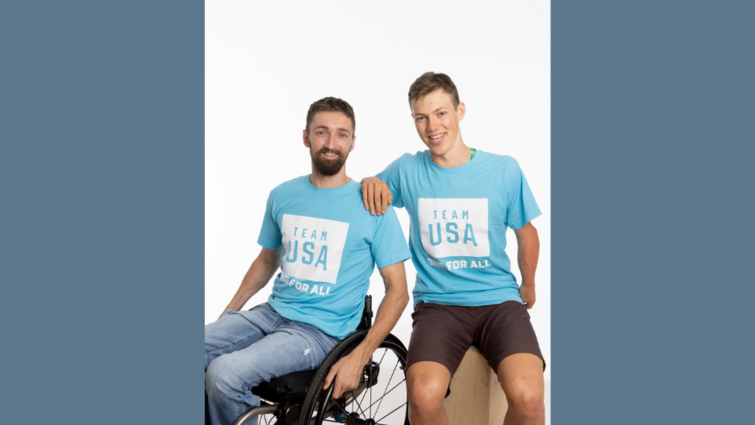two Caucasion males, one in a wheelchair in blue t-shirts