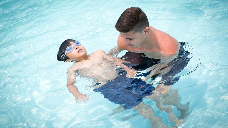 Man helping young boy float in swimming pool