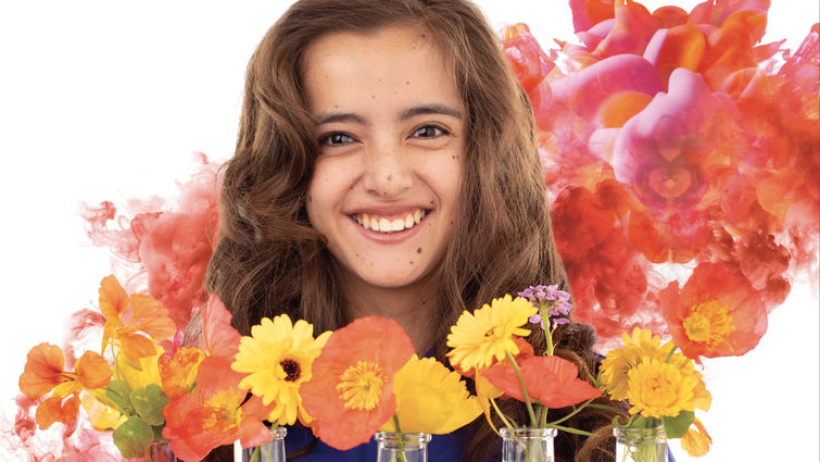 teenage caucasian female smiles in front of vases of flowers