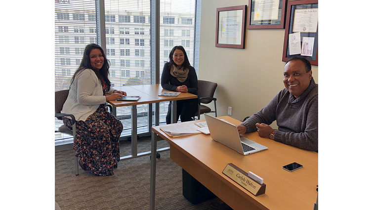 Two women and one man sit in office with large window