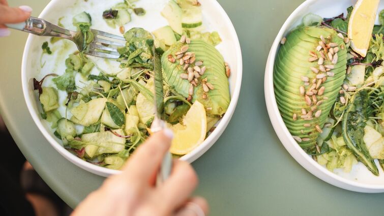 Overhead view of a woman eating a green salad with avocado, cucumber and toasted sunflower seeds 