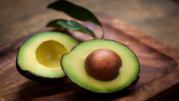 Avocado cut in half on a wood cutting board.