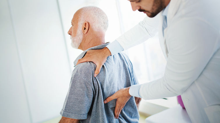 physician checks elderly mans back for pain