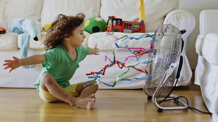 Child sitting in front of fan inside home